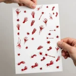 Hand holding a sheet of bloody handprint stickers showing scale
