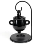 Black ceramic witch cauldron oil burner hanging on a metal stand, front studio view