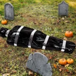 Fake corpse Halloween prop styled with tombstones and autumn leaves