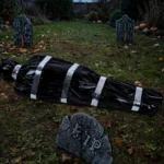 Fake corpse prop in a garden graveyard scene with tombstones at dusk