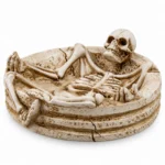 Resin skeleton ashtray with full skeleton lounging in a stone dish, front view