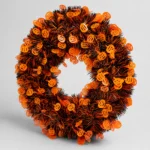 Orange and black Halloween tinsel door wreath with pumpkin cut-outs, three-quarter angle